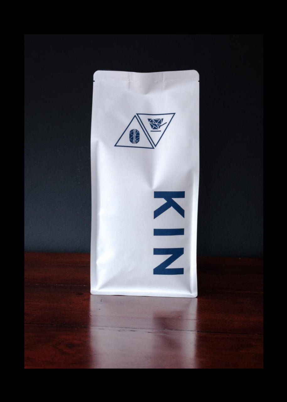 White coffee bag with 'KIN' branding. Premium coffee beans with a glossy roast, crafted for coffee lovers who savor every sip